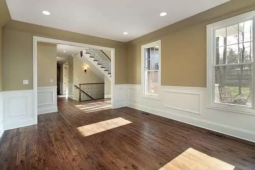 Engineered hardwood flooring in a room with brown patterned planks, beige walls, and a staircase.