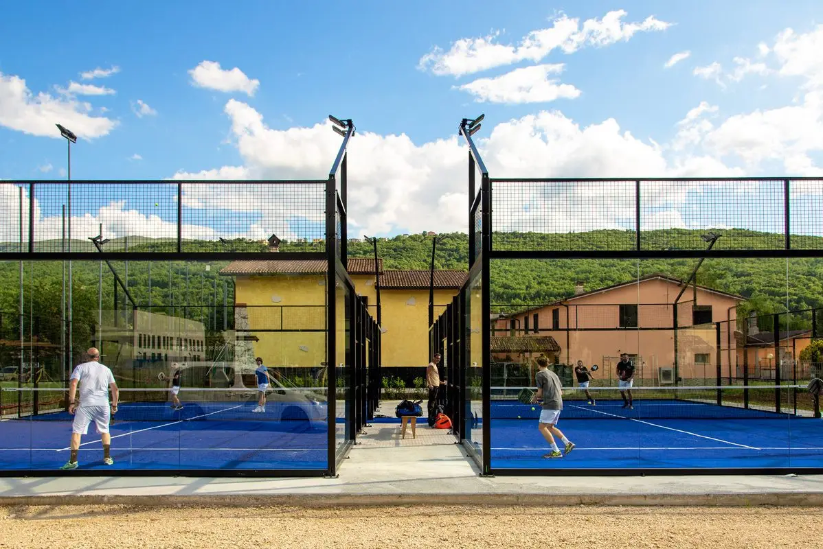 Two padel tennis courts with players engaged in a match under a blue sky.