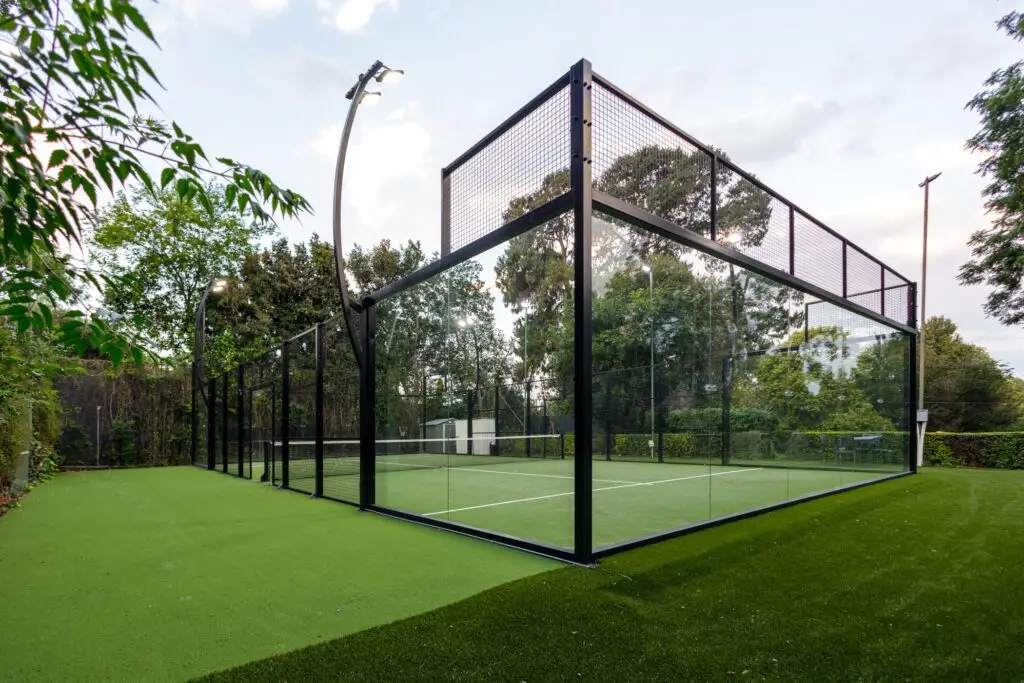 Modern paddle tennis court featuring glass walls and artificial turf