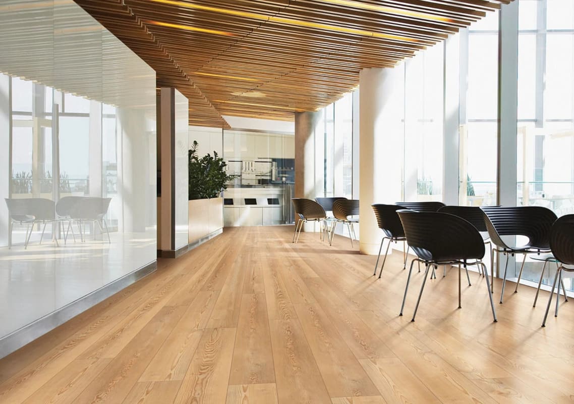 Bright wood-plank flooring in a modern, sunlit office with glass walls, a slatted wood ceiling, and black chairs; no people.