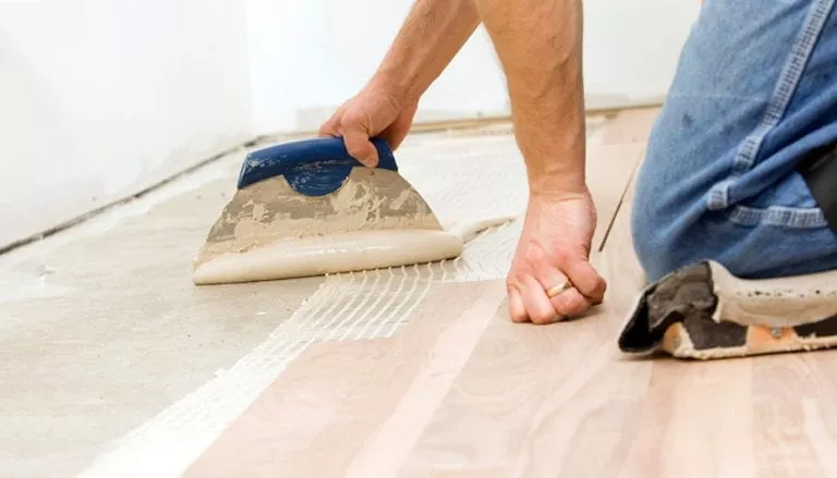 Man applying glue to a subfloor as a moisture barrier during installation