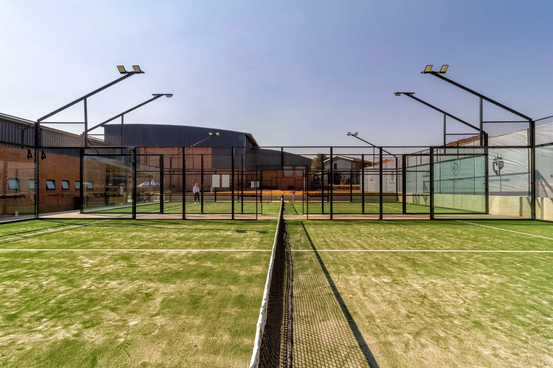 Two padel tennis courts with artificial turf and glass walls under a clear sky.